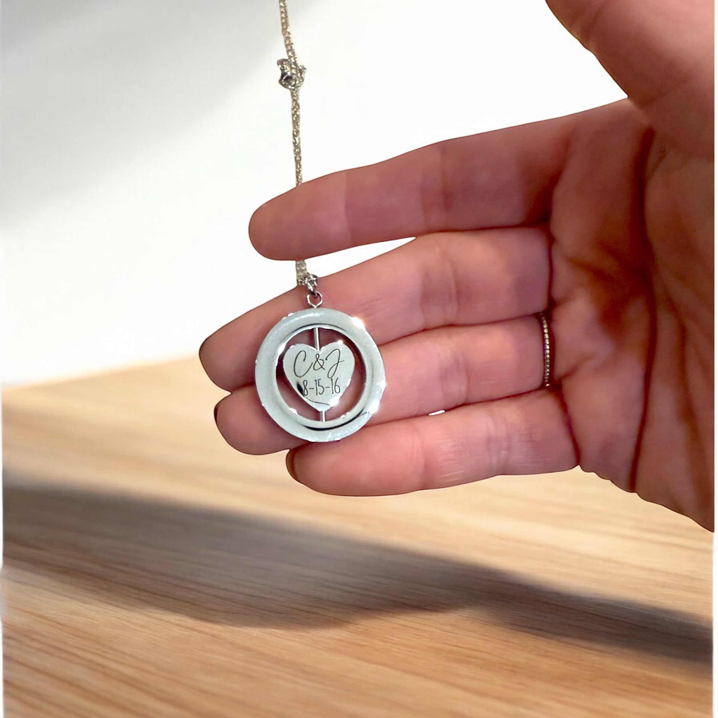 Hand holding a silver necklace with a round pendant on a wooden surface