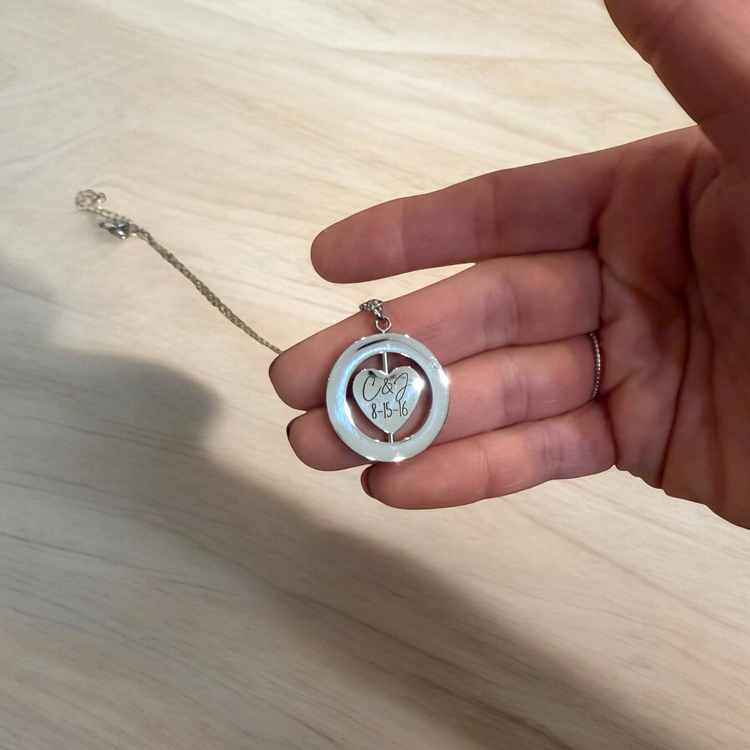 Hand holding a silver pendant with engraved text on a wooden surface
