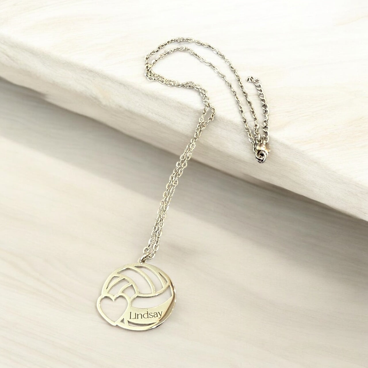 A personalized necklace with a pendant featuring a volleyball design and the name "Lindsay" engraved on it.