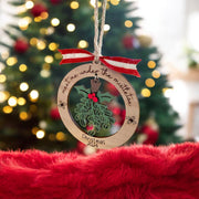 A wooden ornament with a holly and mistletoe design hangs on a string, with a red ribbon and the text "Meet me under the mistletoe" and "Christmas 2021" written on it.