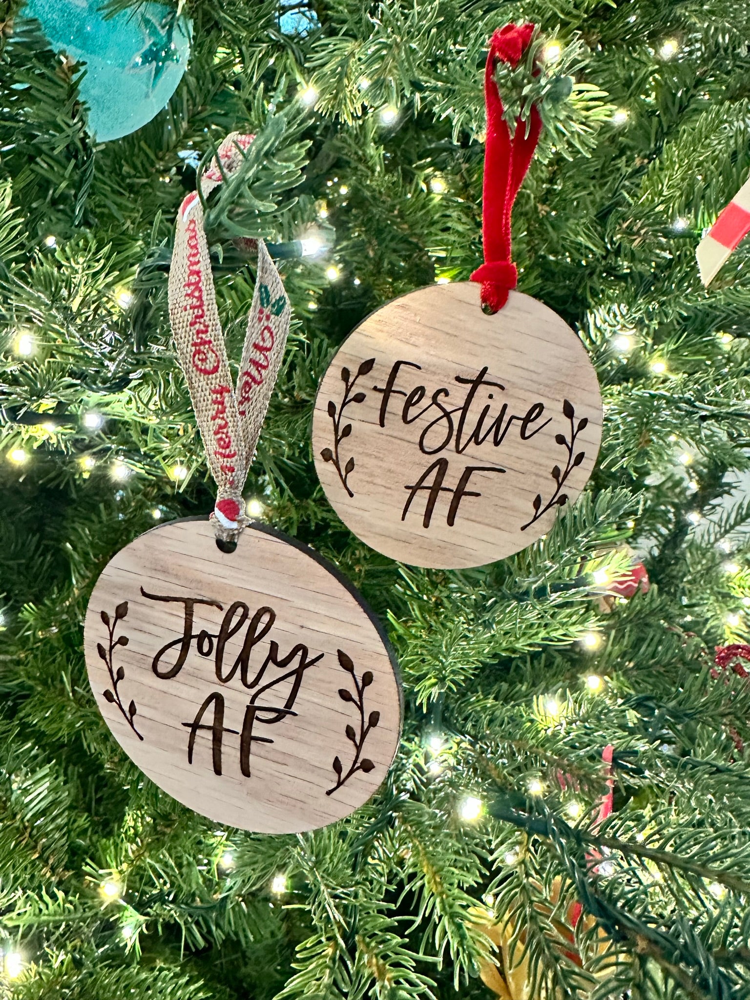 a Christmas tree decorated with two wooden ornaments hanging from the branches. The ornaments have the text "Jolly AF" engraved on them, which appears to be a humorous take on the phrase "Festival AF".