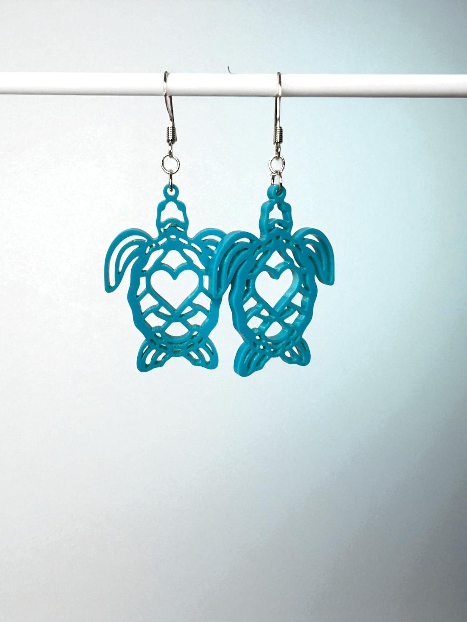 A pair of turquoise earrings with heart-shaped cutouts hanging from a white hook.