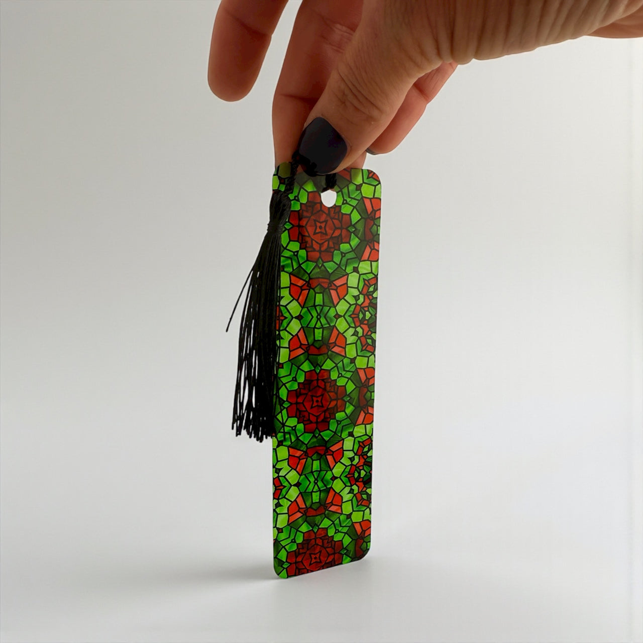 A hand holding a colorful, patterned bookmark with a tassel attached.