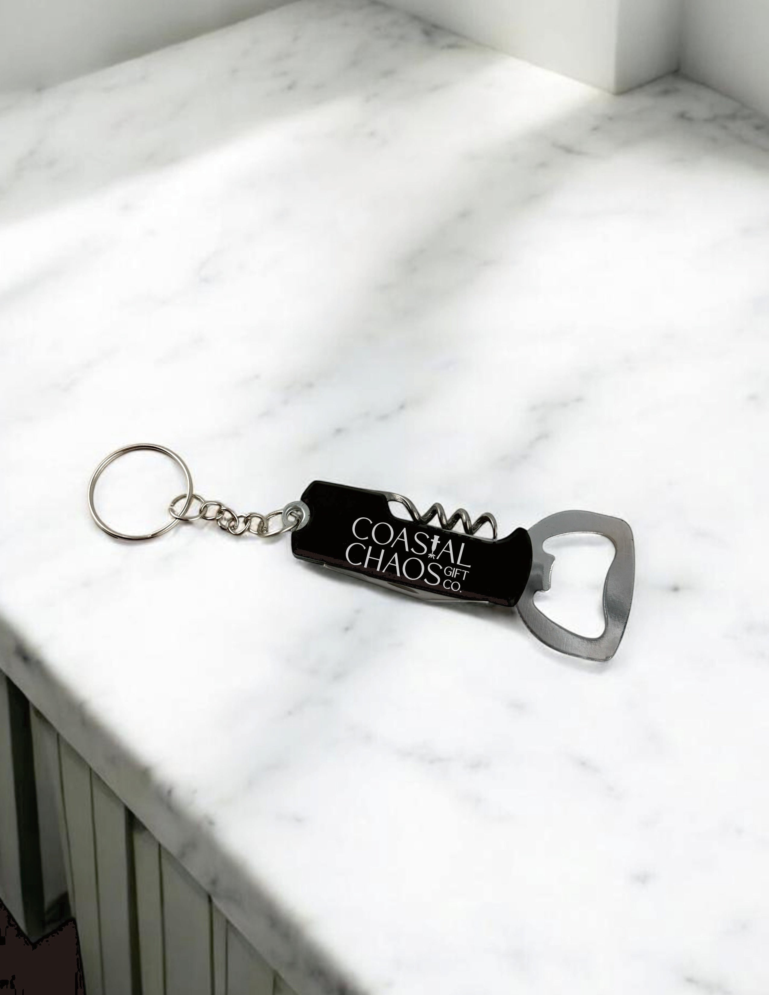 Coastal Chaos Co. black metal multi-tool keychain with corkscrew and bottle opener, engraved logo.