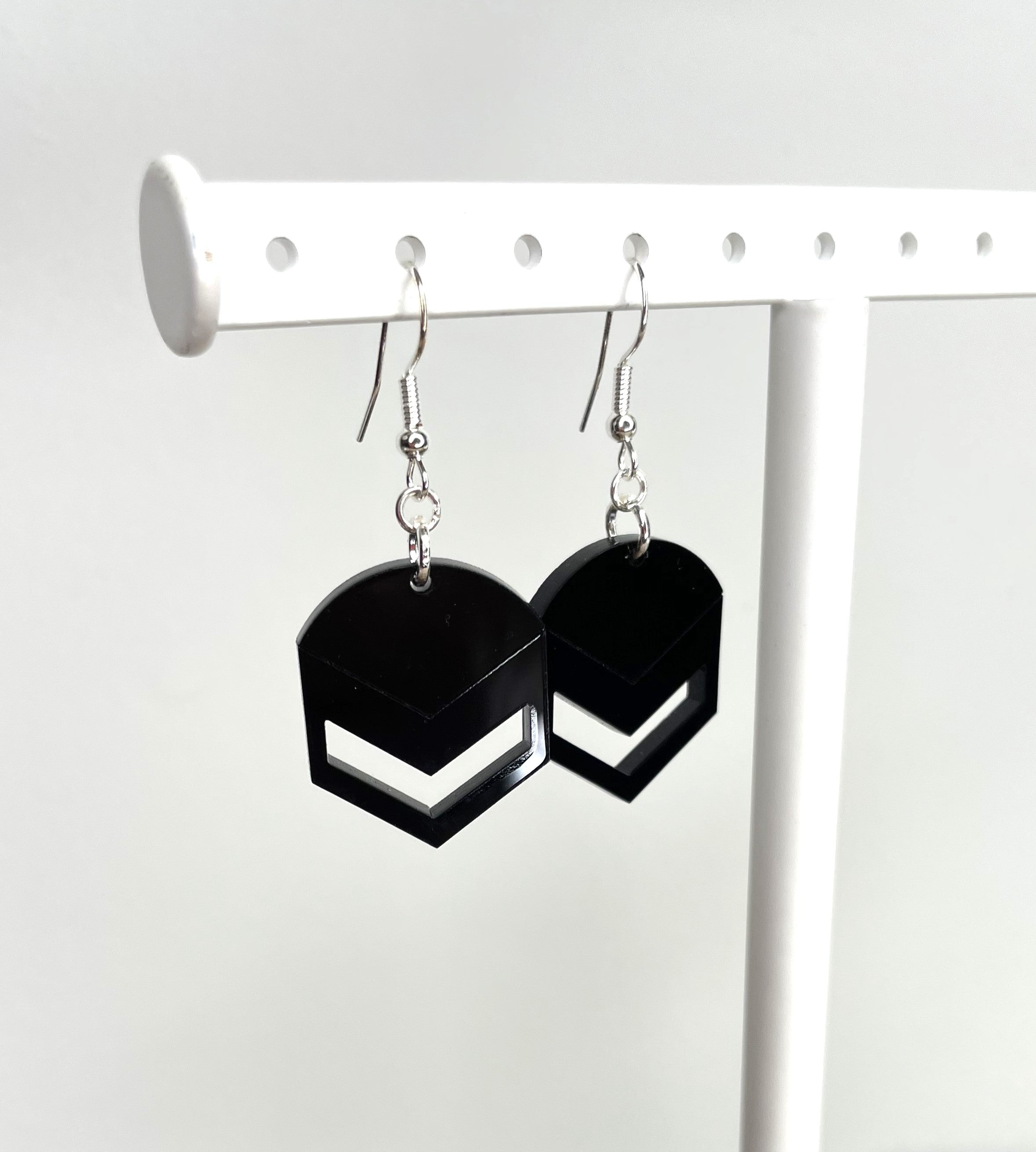 A pair of black geometric earrings with a hexagonal shape and a white line through the center, hanging from a white earring holder.