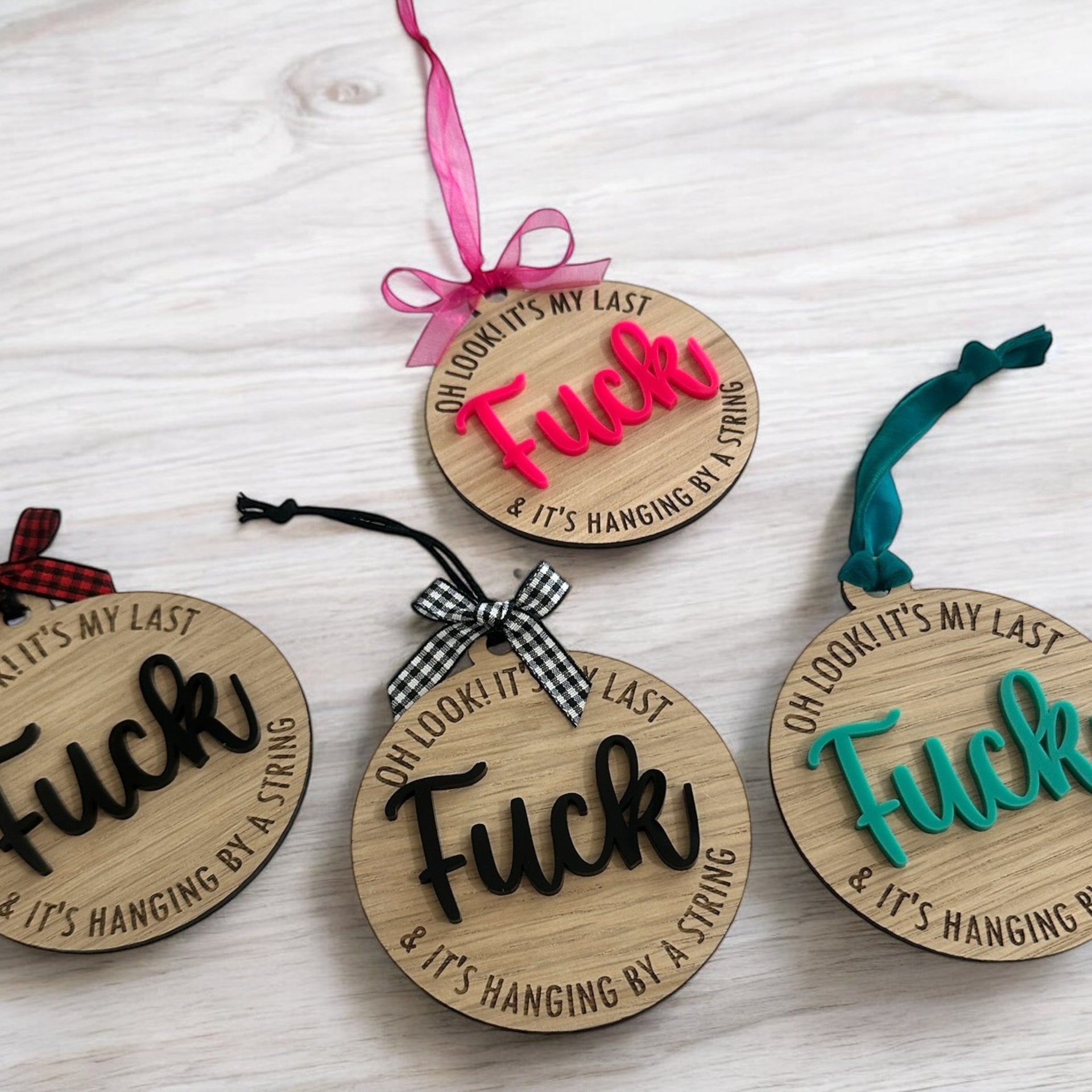 four wooden ornaments with the word "FUCK" written on them, each with a different color ribbon attached.