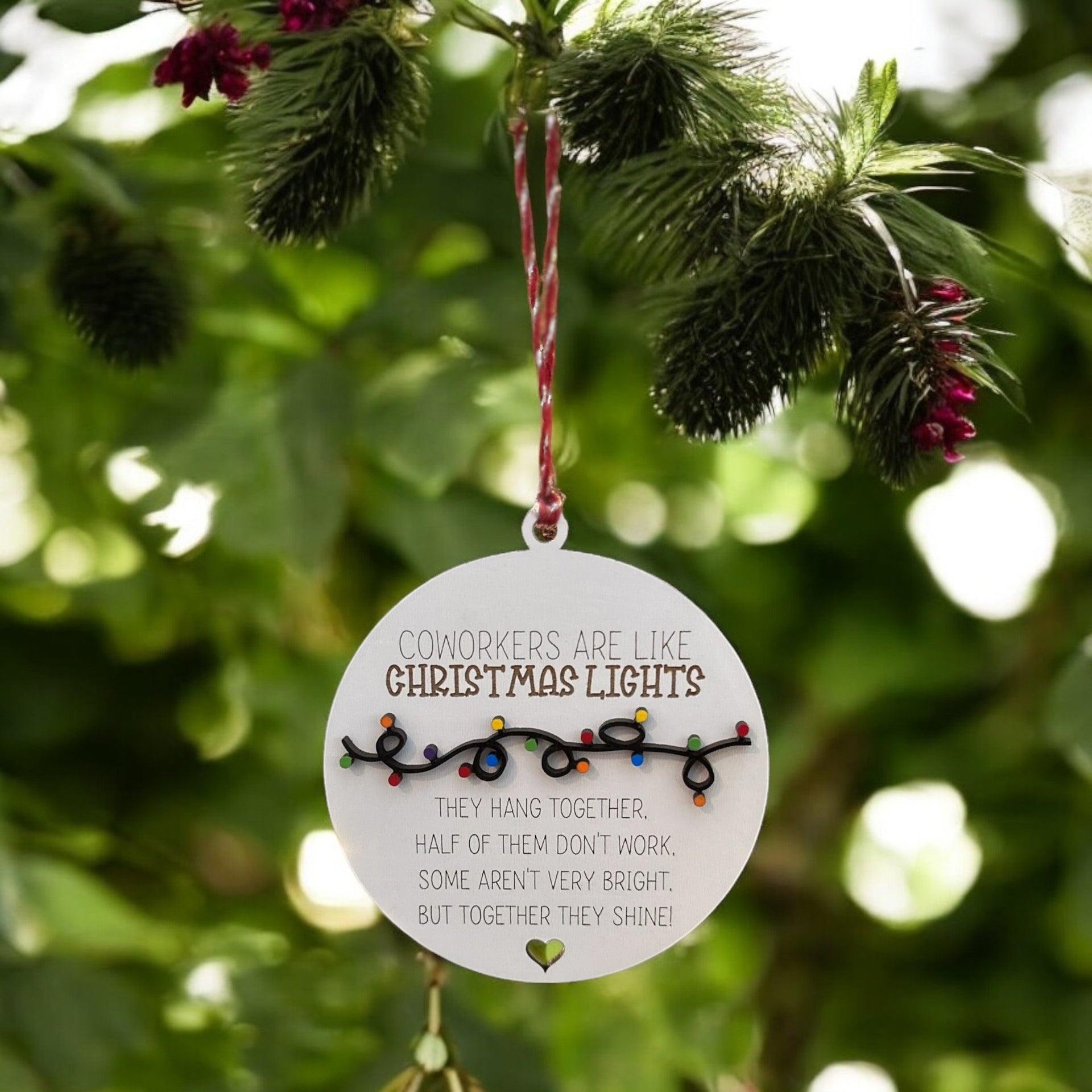 a round ornament hanging from a tree branch with a message about coworkers being like Christmas lights.