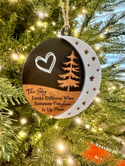 A Christmas ornament hanging on a tree, featuring a heart symbol, a crescent moon, and a pine tree design.