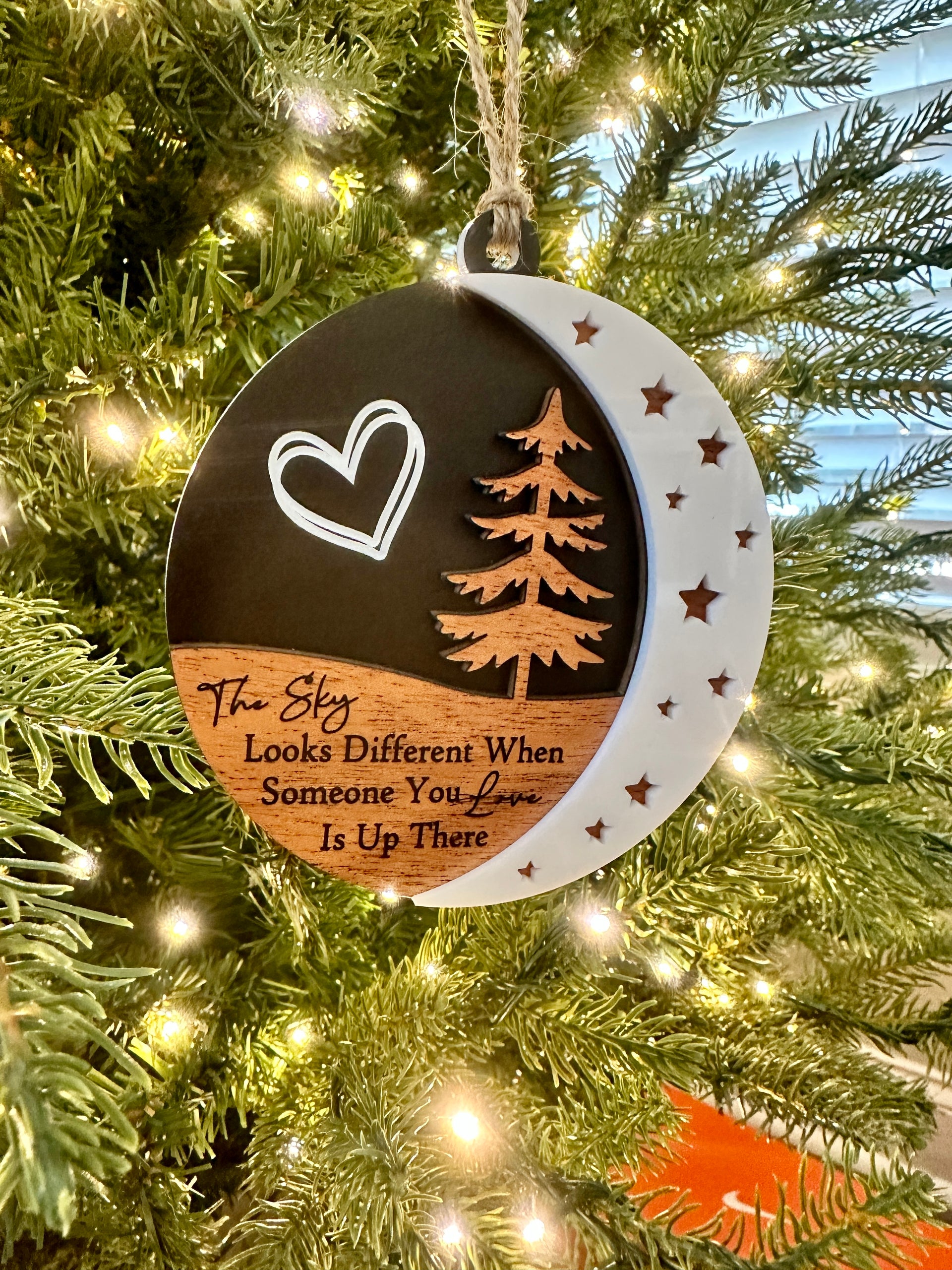 A Christmas ornament hanging on a tree, featuring a heart symbol, a crescent moon, and a pine tree design.