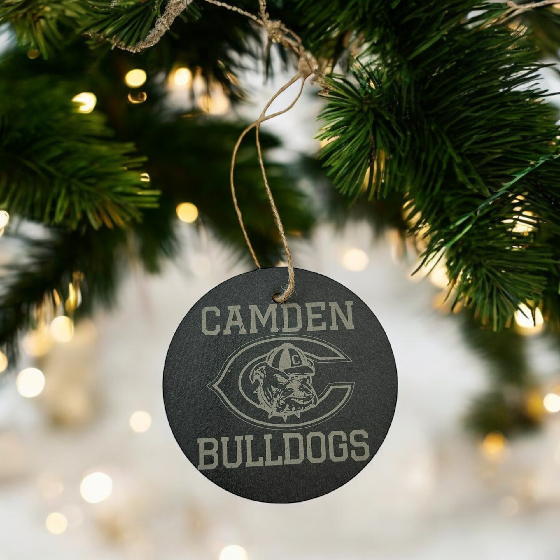 A black ornament with the word "CAMDEN" and a bulldog logo is hanging from a Christmas tree branch.