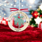 A wooden ornament with a Christmas tree and mistletoe hangs on a string, with a red ribbon and the text "Meet me under the mistletoe" written on it.