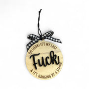 A wooden ornament with the text "OH LOOK! IT'S MY LAST FUCK & IT'S HANGING BY A STRING" engraved on it.