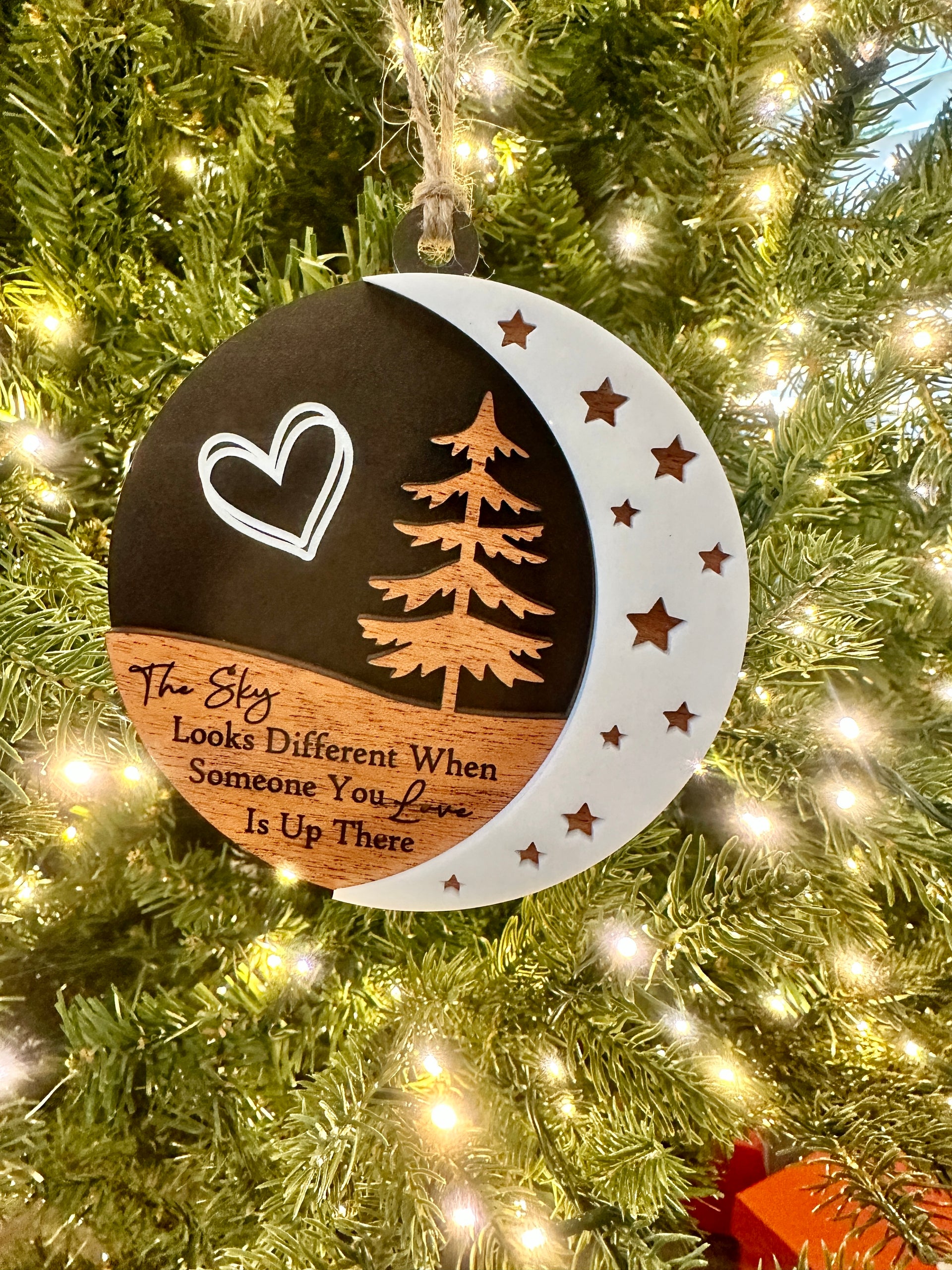A Christmas ornament hanging on a tree, featuring a crescent moon and a tree silhouette.