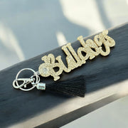 A gold glitter keychain with the word "BULLHOG" written on it, resting on a wooden surface.