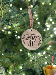 A wooden ornament with the text "Folly AF" hangs from a Christmas tree, surrounded by twinkling lights.